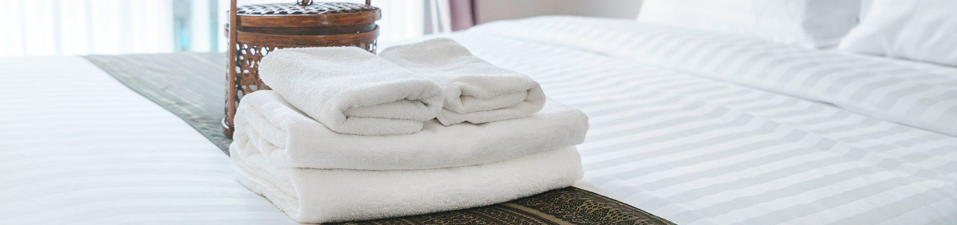 Ein Hotelbett mit elegantem Läufer, Handtüchern und Körbchen